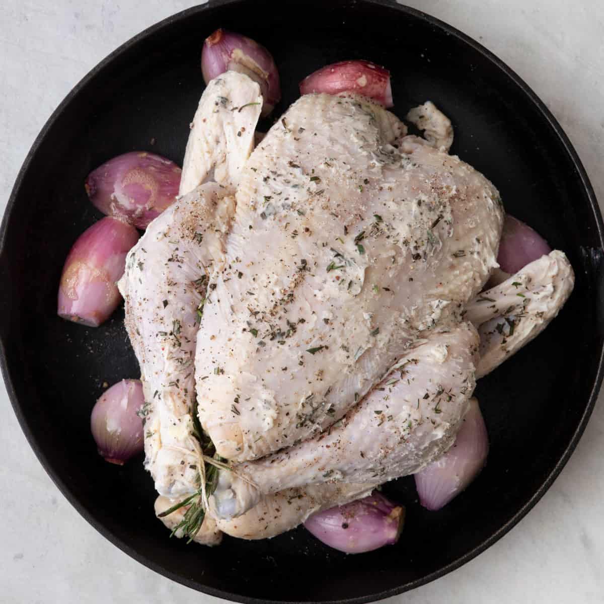 Whole seasoned chicken placed on top of scallions in cast iron pan before baked.