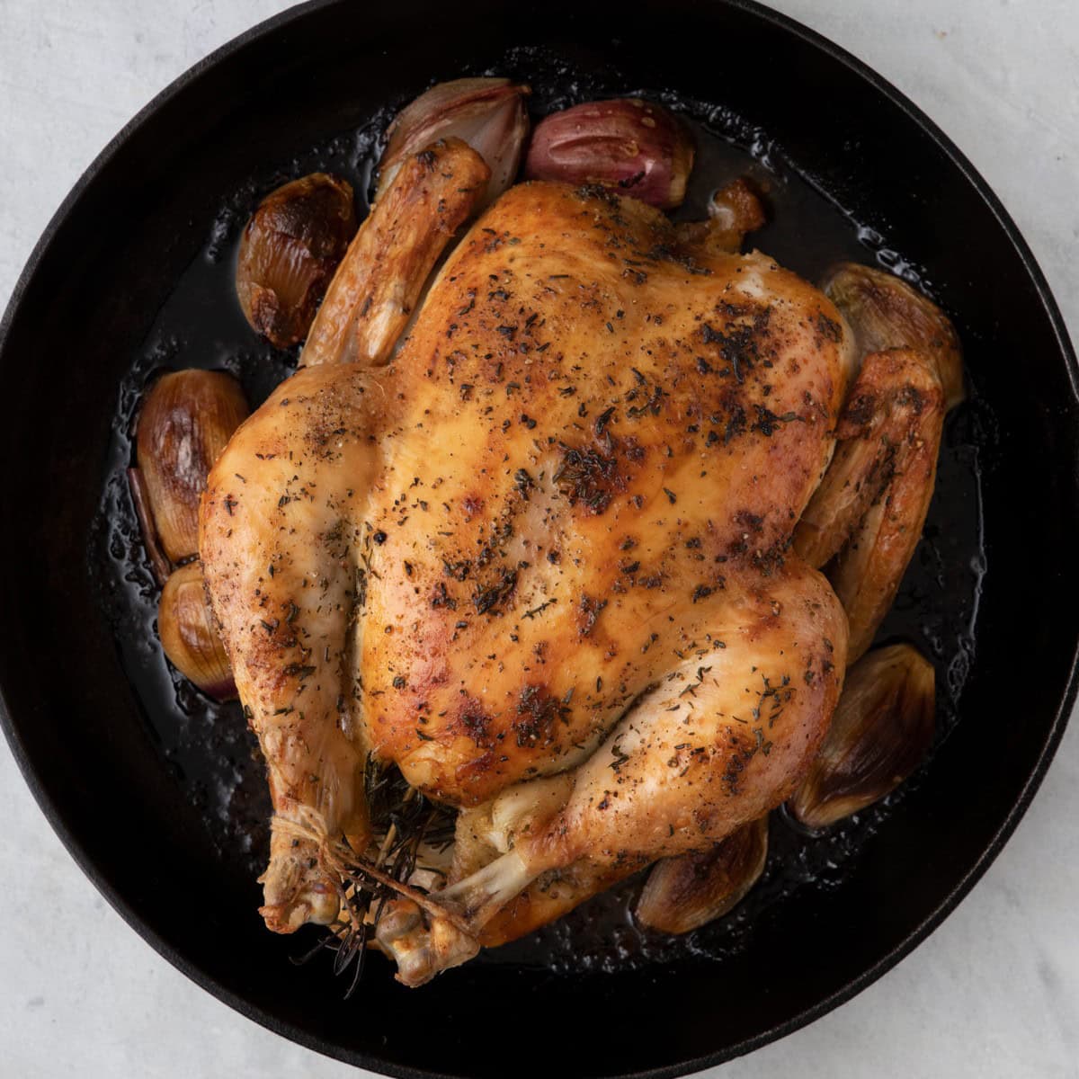 Whole seasoned chicken placed on top of scallions in cast iron pan after baked.