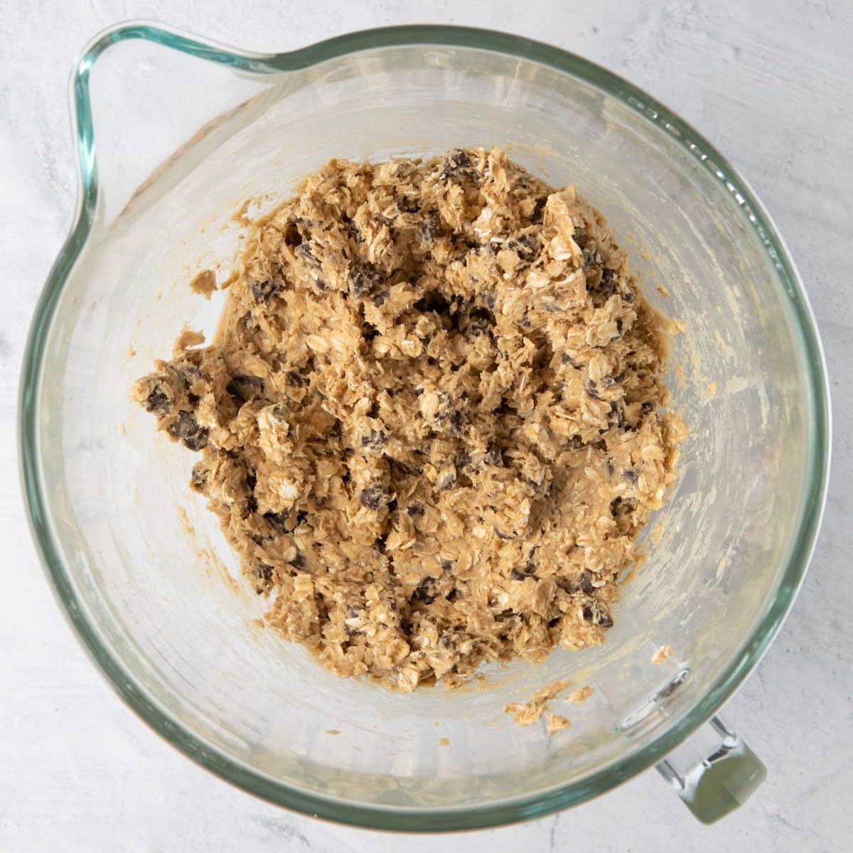 Cookie dough with rolled oats and chocolate chips mixed in in the bowl of a stand mixer.