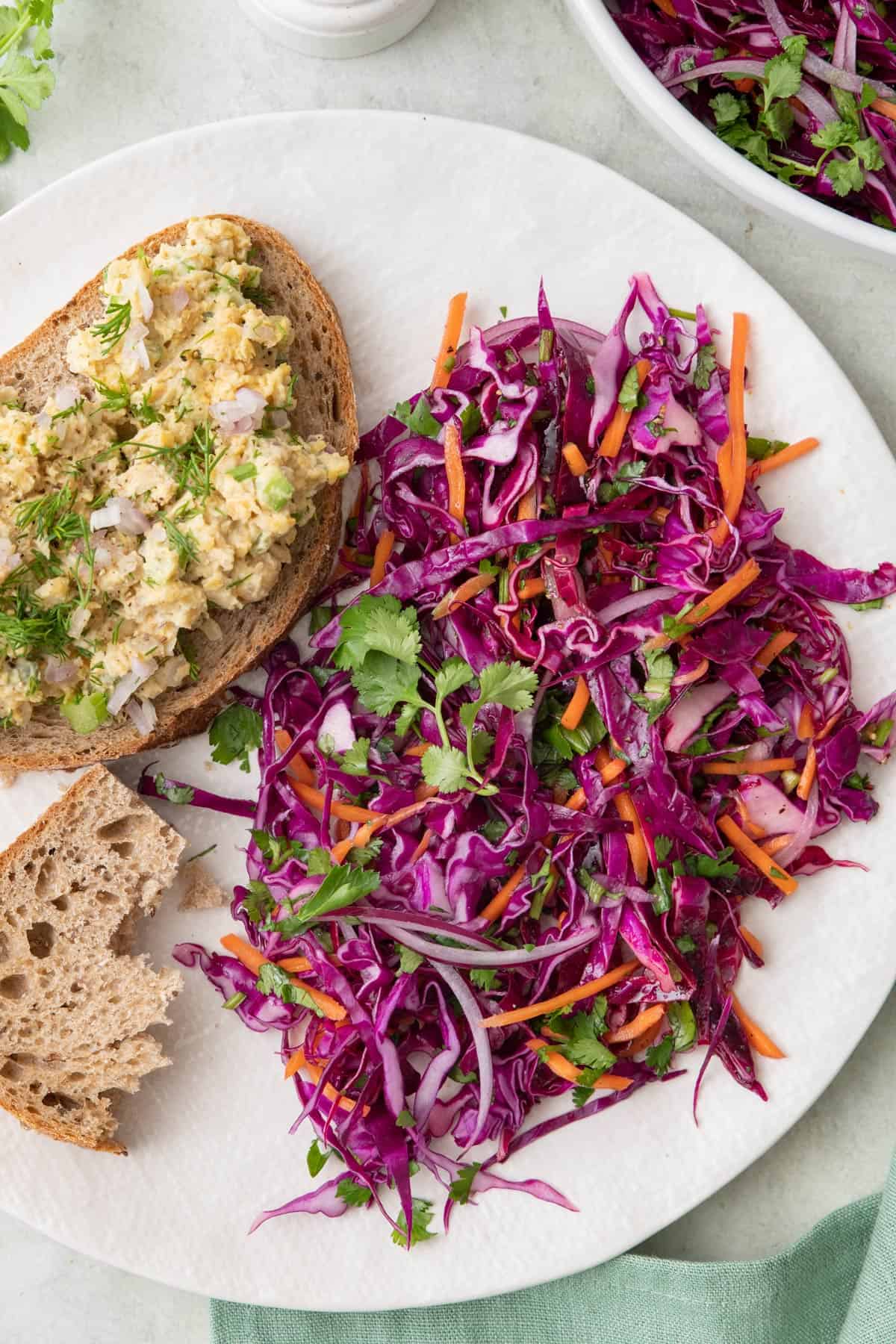 Large portion of red cabbage slaw on plate with half an open-faced chickpea salad sandwich next to it.