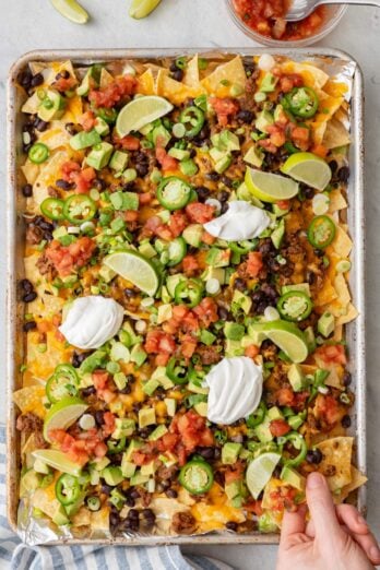 Hand lifting up a few chips from the Sheet Pan Nachos.