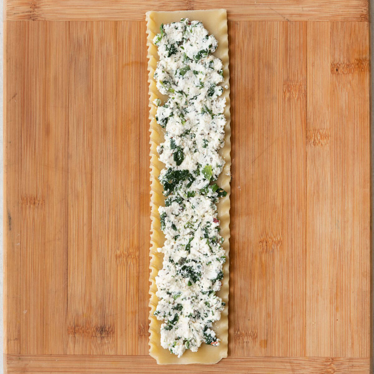 Lasagna noodle on work surface with 2 tablespoons filling spread evenly over it.