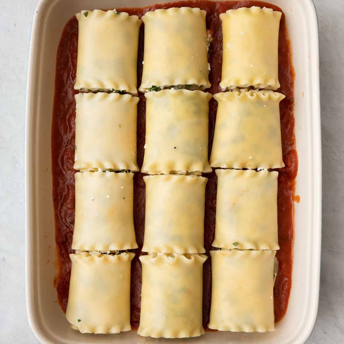 Lasagna roll ups placed on top of sauce in baking dish, 4 rows with 3 in each row.