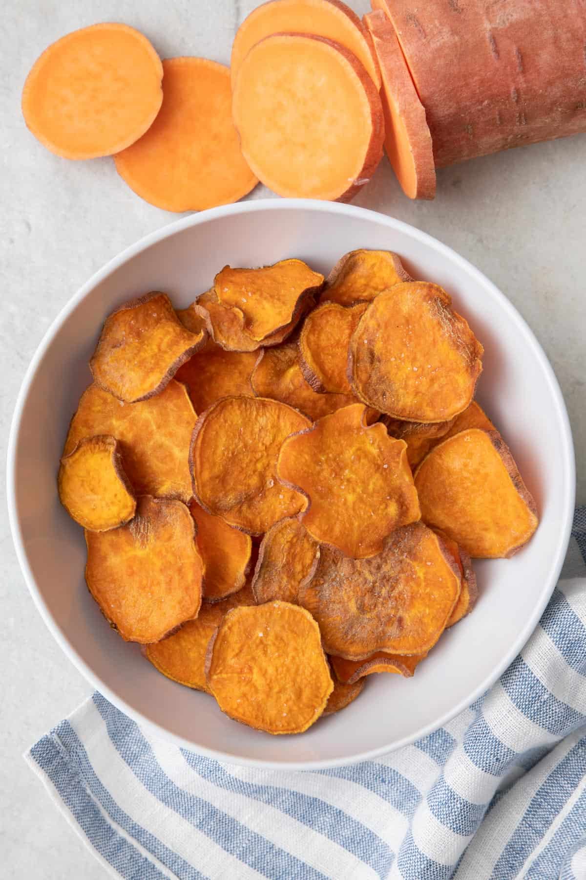 Bowl of sweet potato chips with a partial sliced sweet potato nearby.