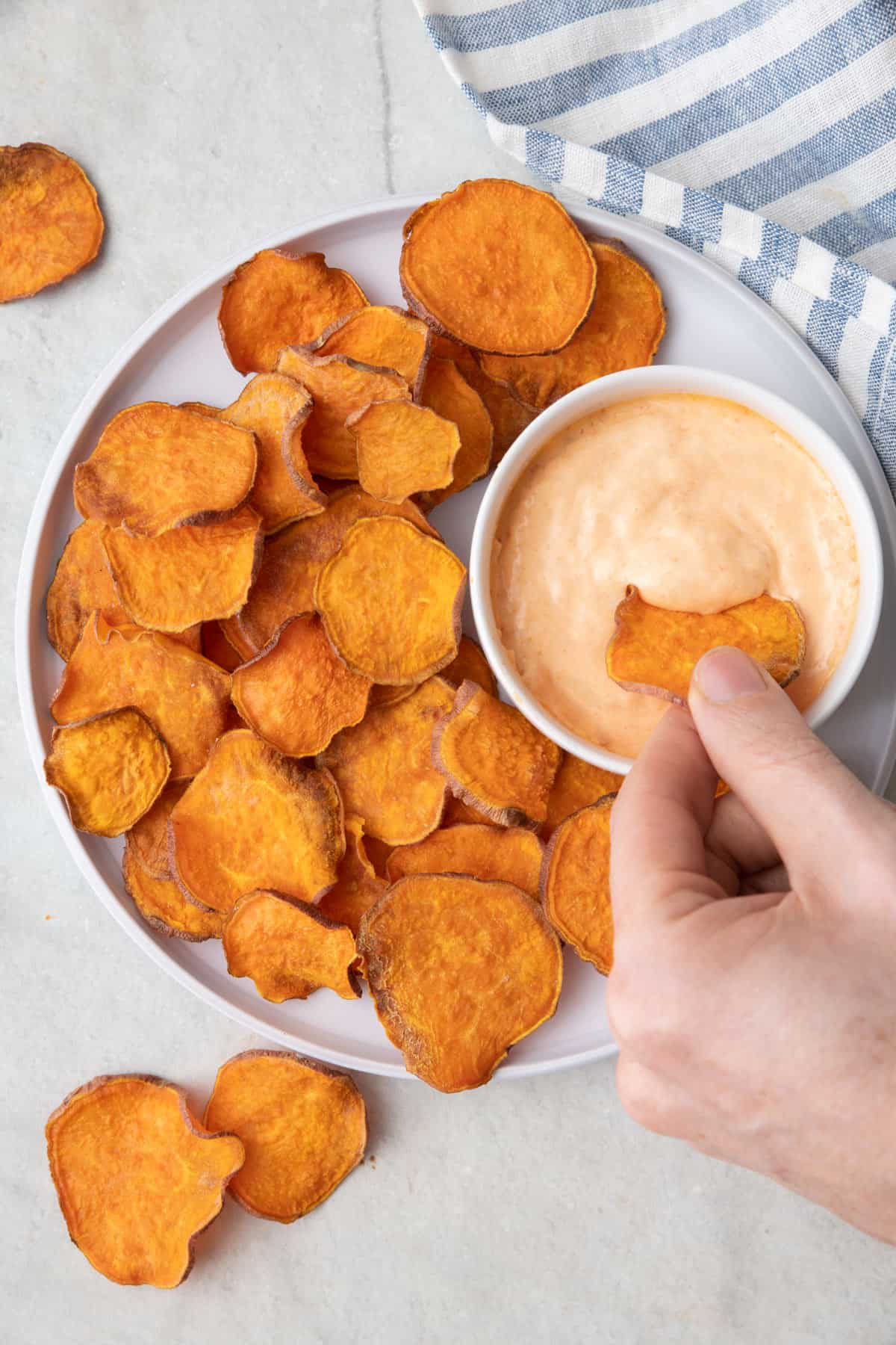 Plate of sweet potato chips with one chip being dipped into spicy mayo.