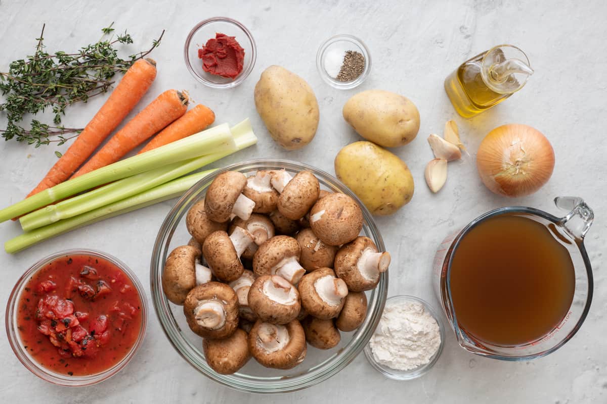 Ingredients for recipe before being prepped: fresh parsley, carrots, celery, diced tomatoes, tomato paste, potaotes, mushrooms, seasoning, flour, garlic cloves, oil, onion, and broth.