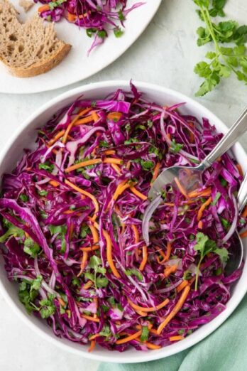 Large bowl of red cabbage slaw with serving set dipped inside.