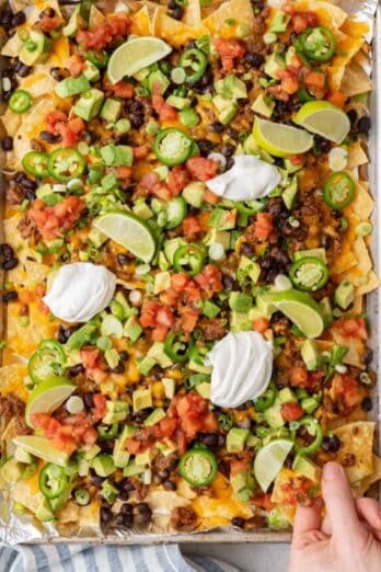 Hand lifting up a few chips from the Sheet Pan Nachos.