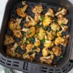 Brown and crispy cauliflower florets in an air fryer basket garnished with fresh parsley.
