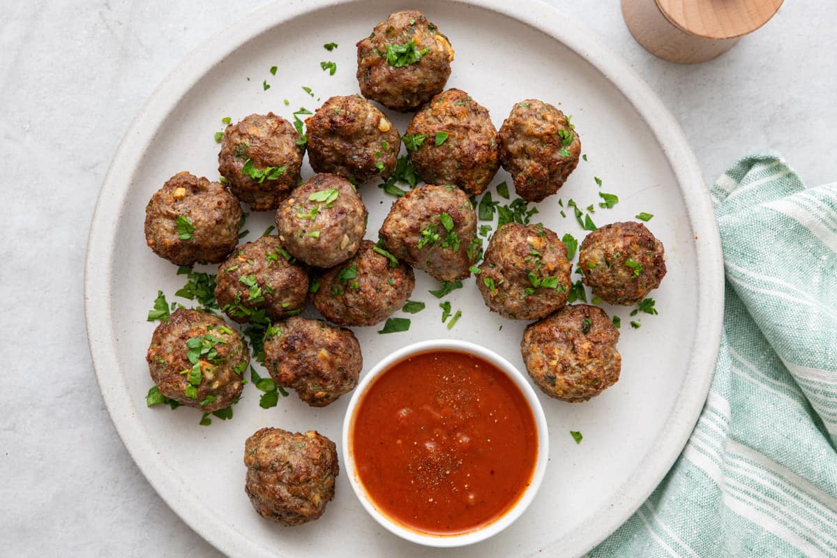 Plate of meatballs garnished with fresh parsley with a small bowl of marinara for dipping.