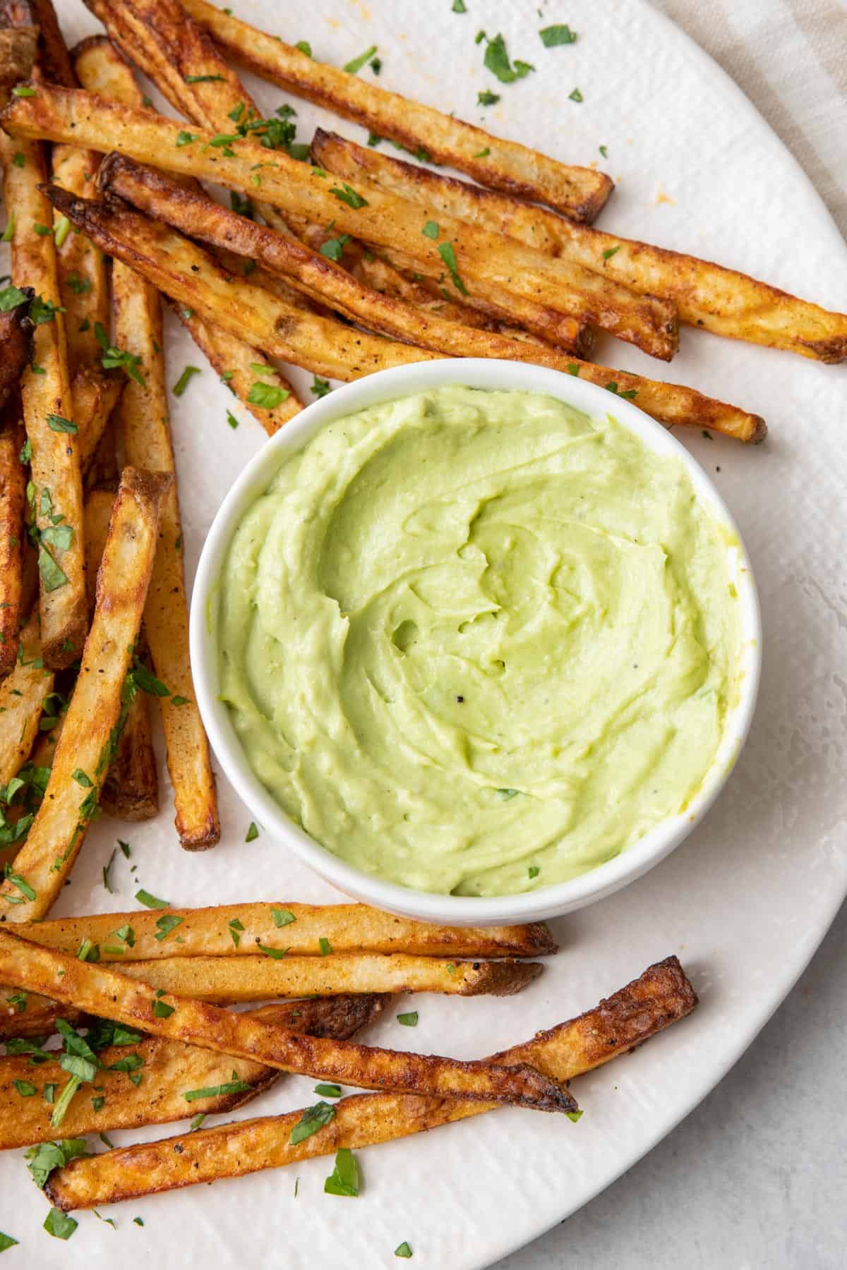 Avocado crema in a small dish on a plate with crispy fries.