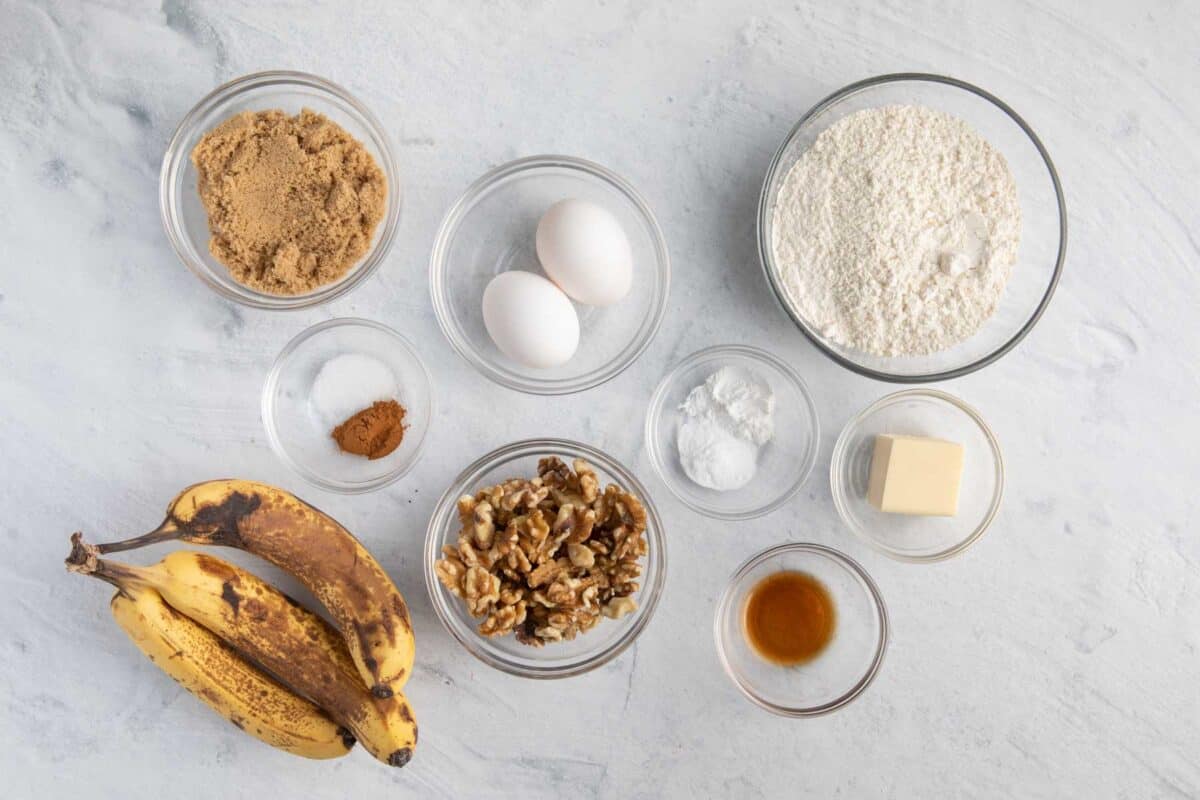 Ingredients for recipe before prepped: brown sugar, salt and cinnamon, 3 ripe bananas, 2 eggs, baking powder and soda, flour, butter, vanilla, and walnuts.