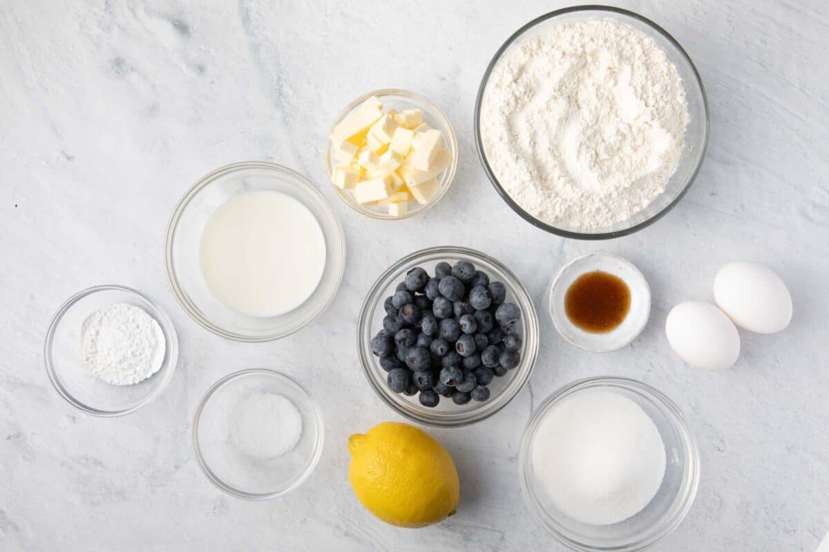Ingredients for recipe: baking powder, milk, salt, butter cubes, fresh blueberries, lemon, flour, vanilla, sugar, and eggs.