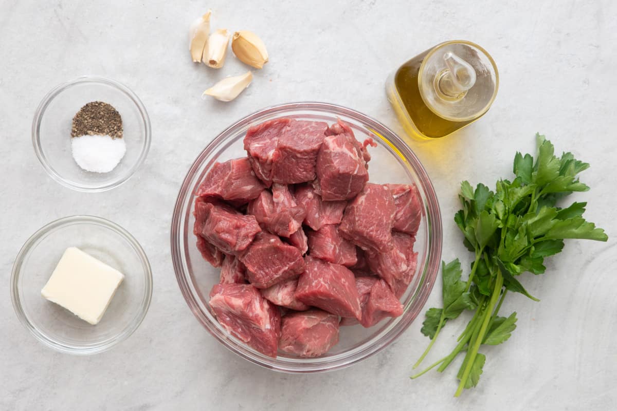 Ingredients before prepped: salt and pepper, square of butter, garlic cloves, beef chunks, oil, and fresh parsley.