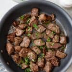 Steak bites in pan garnished with fresh chopped parsley.