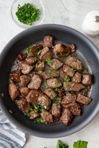 Steak bites in pan garnished with fresh chopped parsley.