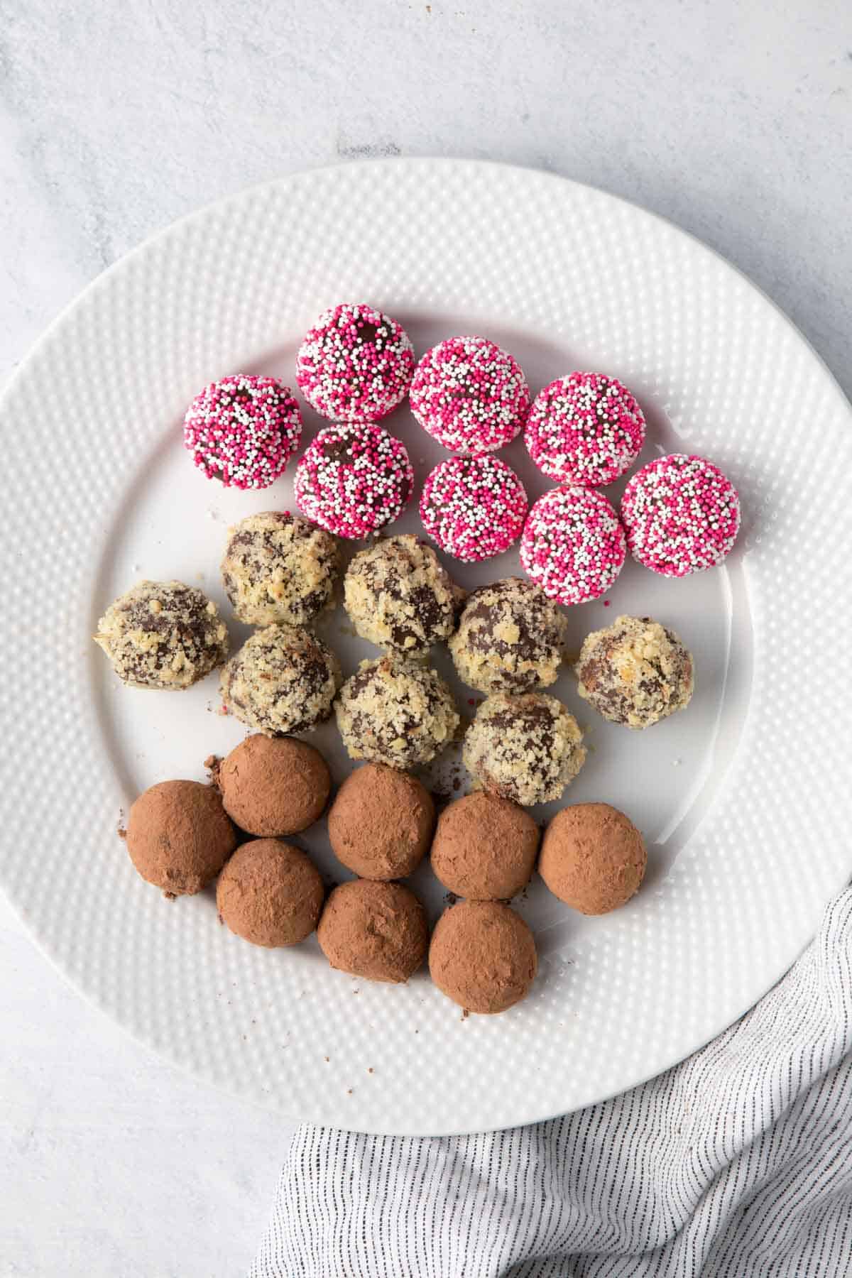 Plat of 24 chocolate truffles with 8 decorated each way: sprinkles, chopped nuts, and cocoa powder.
