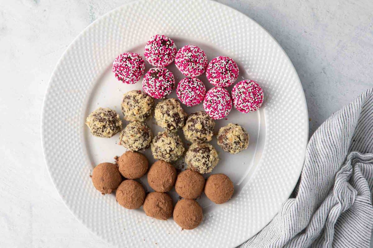 Large plate with decorated chocolate truffles: sprinkles, chopped walnuts, and cocoa powder.