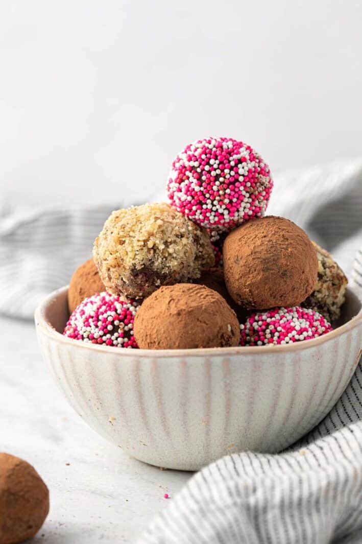 Homemade chocolate truffles decorated three different ways stacked in a bowl with a few next to it.