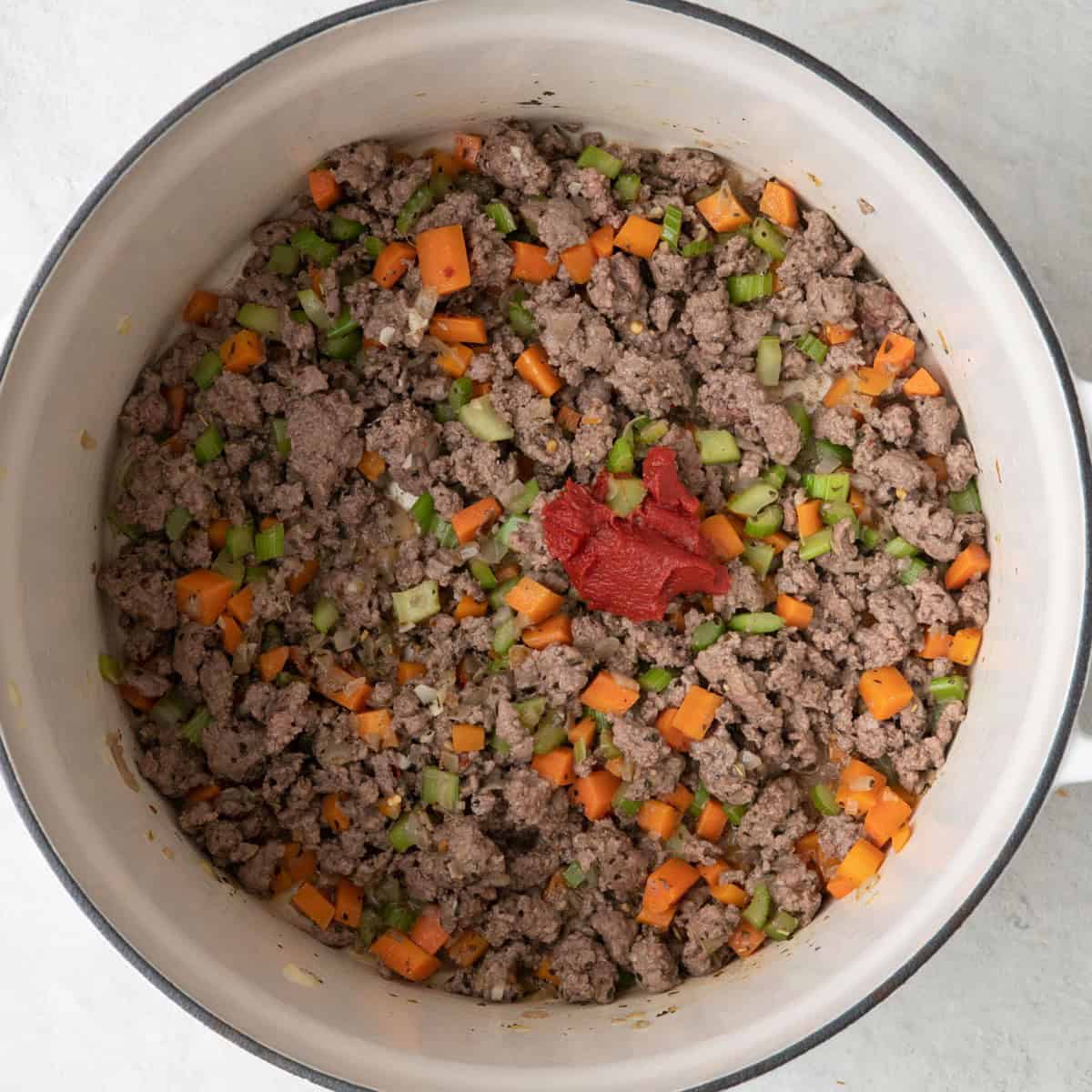 Tomato paste added to cooked ground beef and vegetables before being mixed in.
