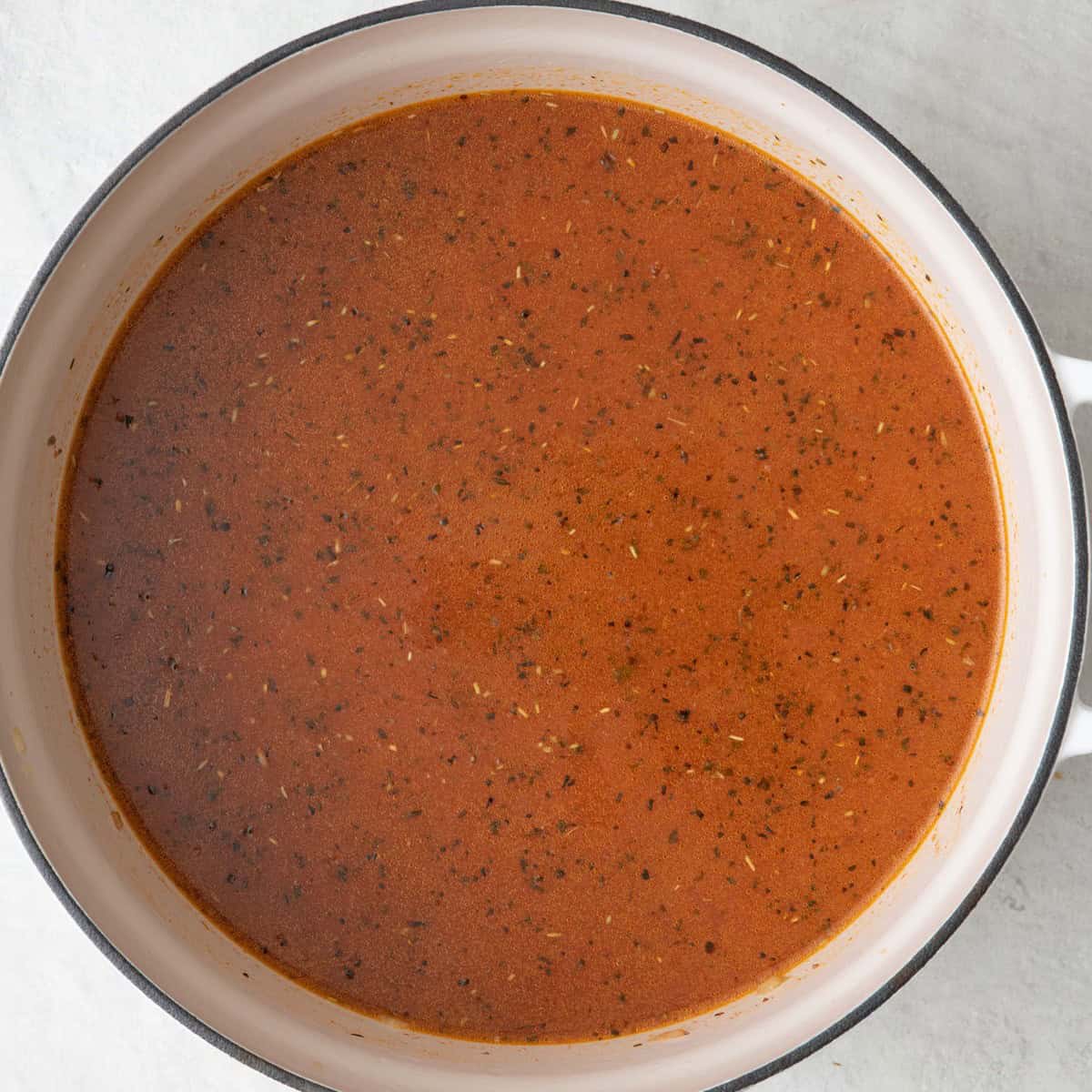 Ground beef with cooked tomato paste in Dutch oven with diced tomatoes, marinara sauce, and broth stirred in.
