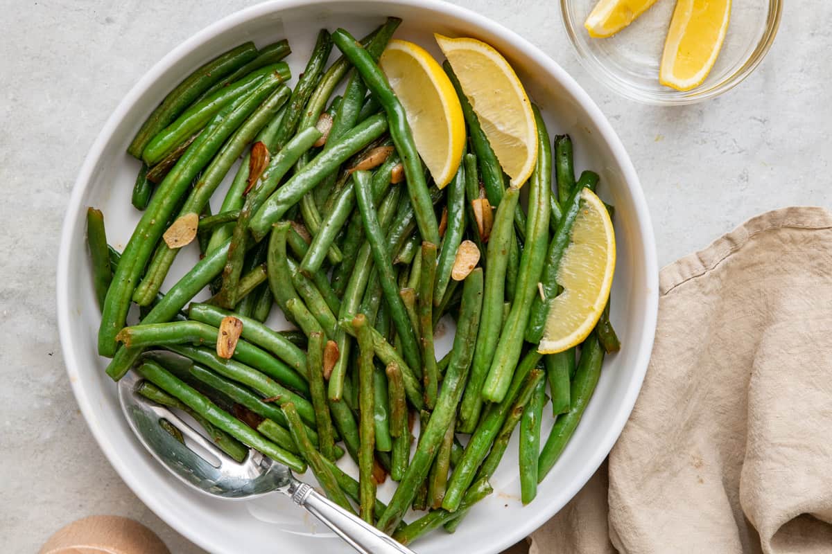 Green beans on a serving platter with serving spoon and lemon wedges.