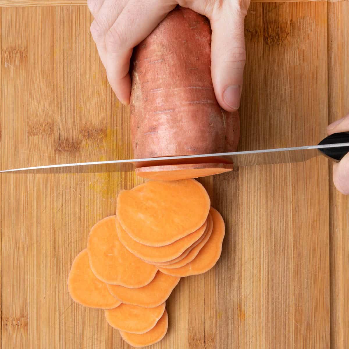 Cutting sweet potato, about halfway through, into thin slices.