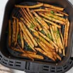Fries in an air fryer basket garnished with fresh parsley.