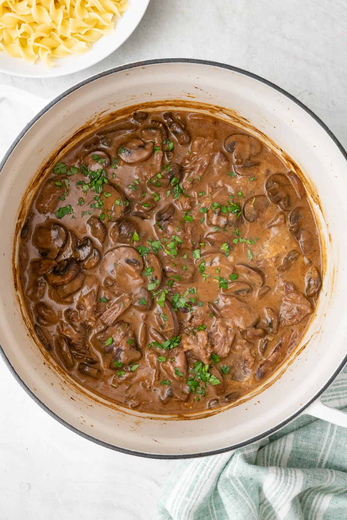 Beef mushroom stroganoff in pot with pasta to the side.