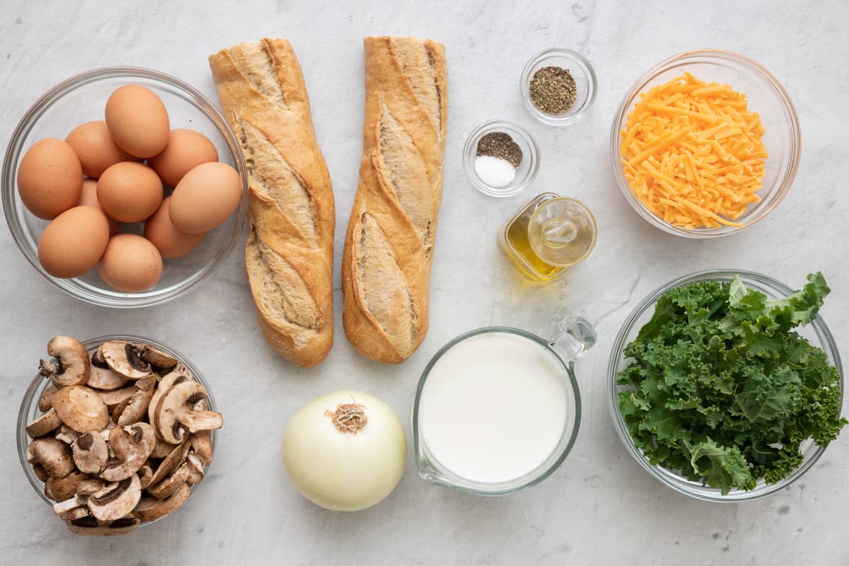 Ingredients for recipe: eggs, sliced mushrooms, French baguette, onion, milk, salt, pepper, seasoning, oil, shredded cheese, an kale.