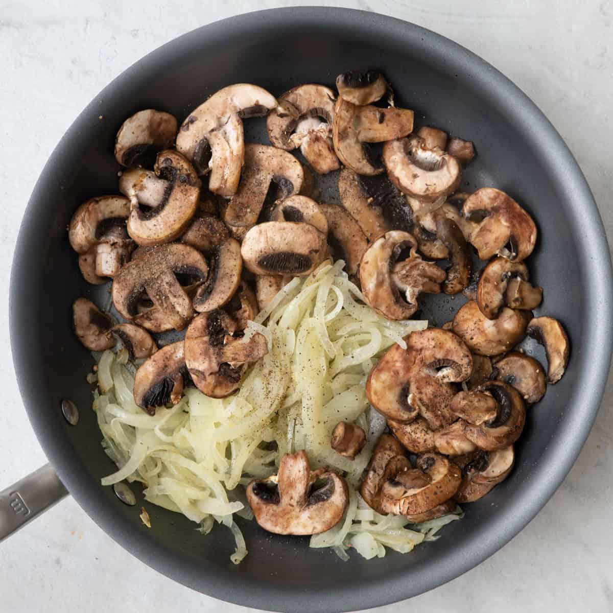 Cooked onions in large saute pan with sliced mushrooms, salt, and pepper added.