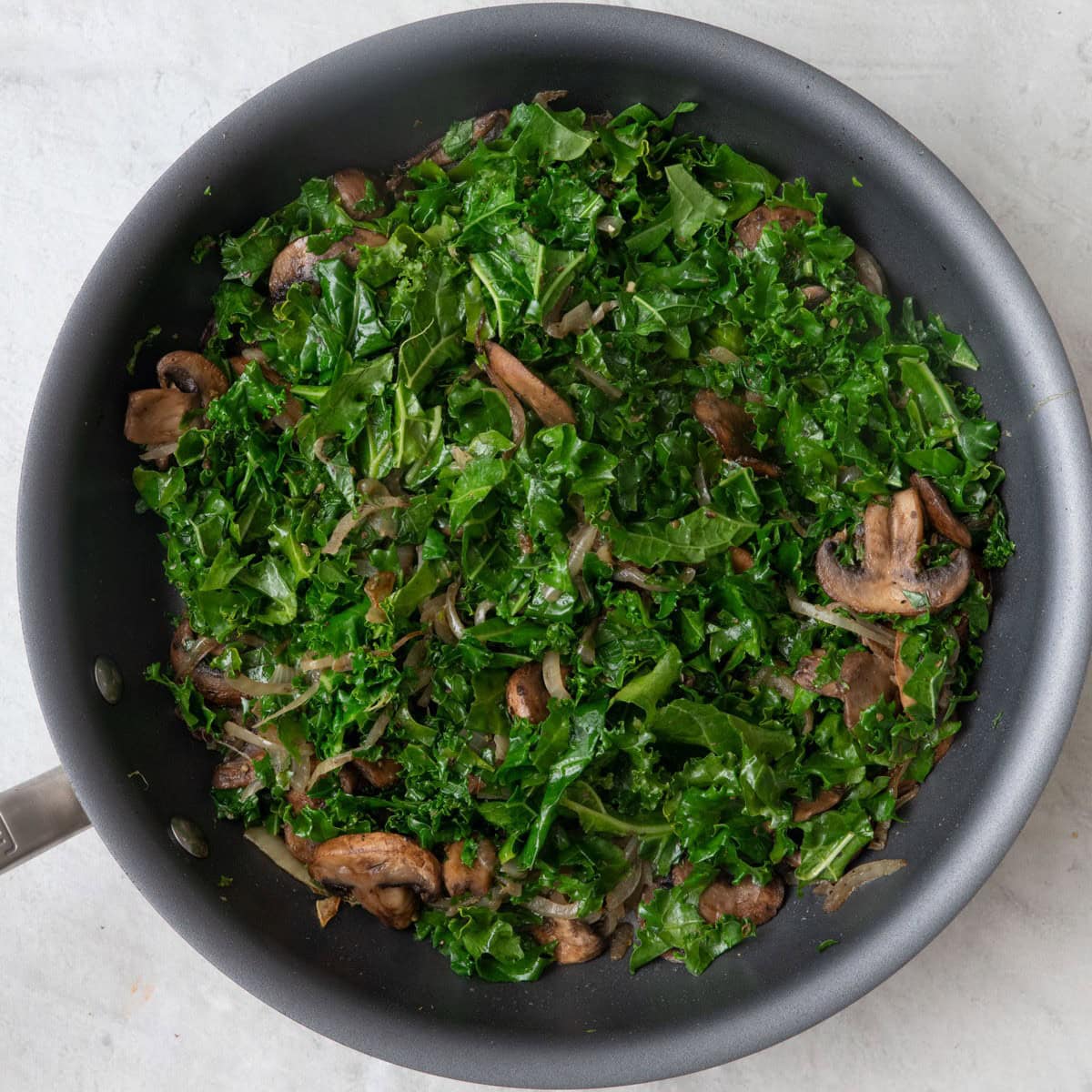 Kale added in with mushroom onion mixture and cooked to show slightly wilted leaves.