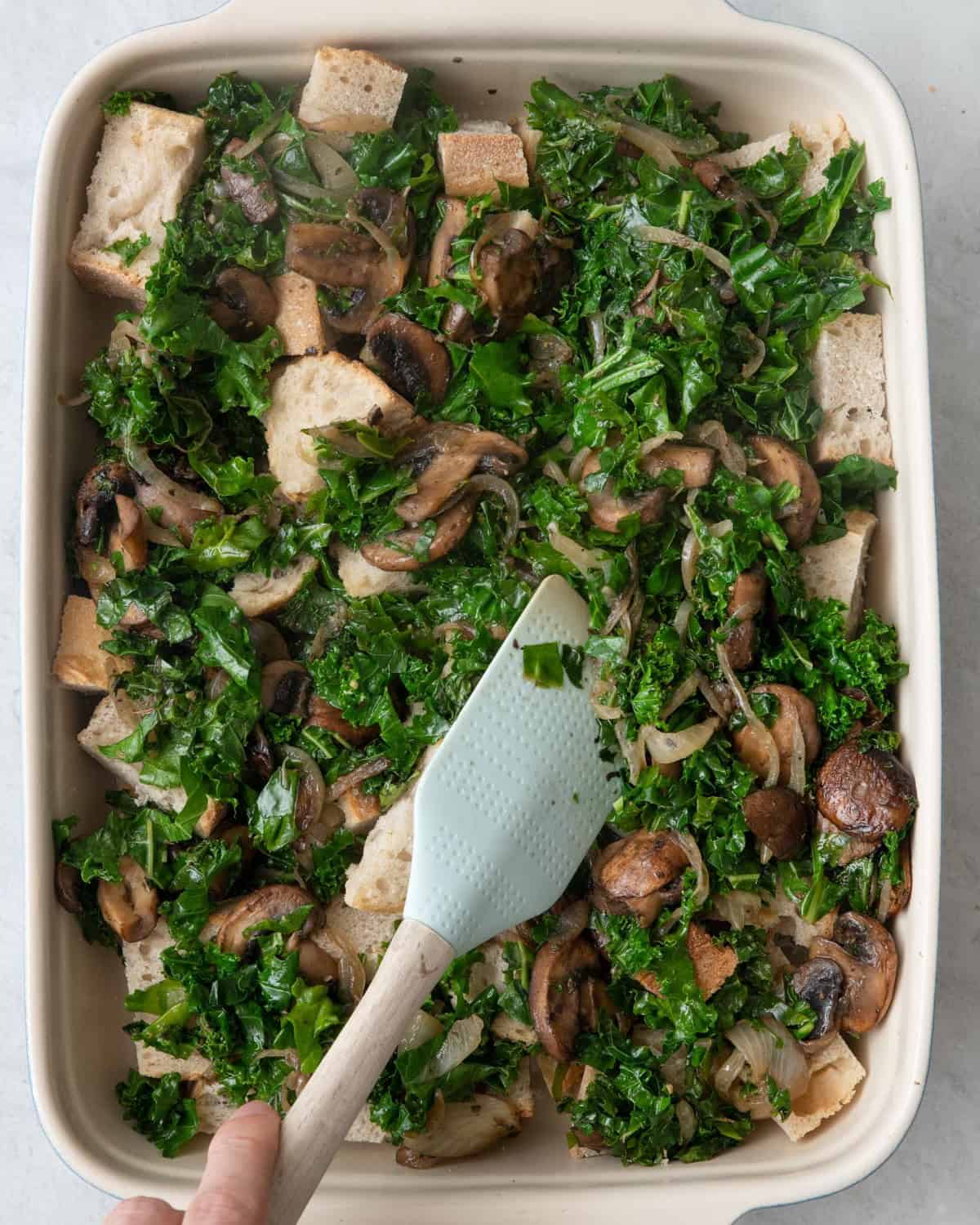 Vegetable mixture being stirred into bread cubes with rubber spatula.
