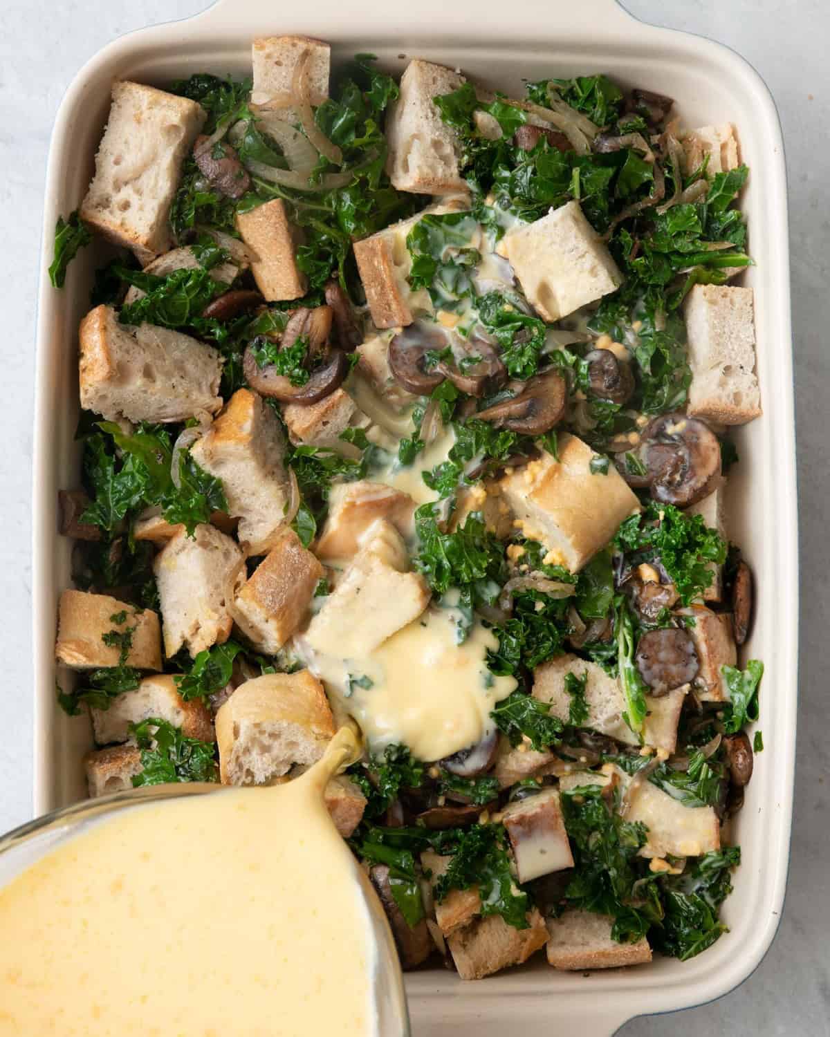 Pouring egg mixture over bread and veggies.