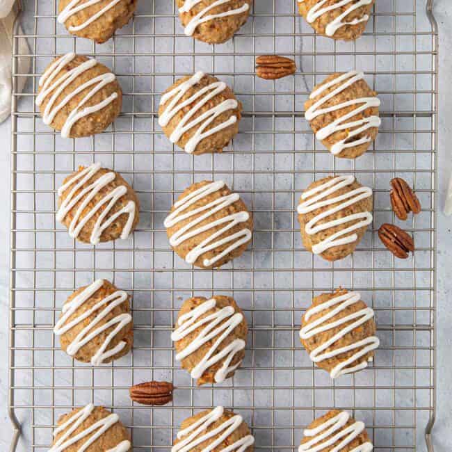 Carrot cake cookies on a wire rack with frosting drizzle and a few pecan halves around.