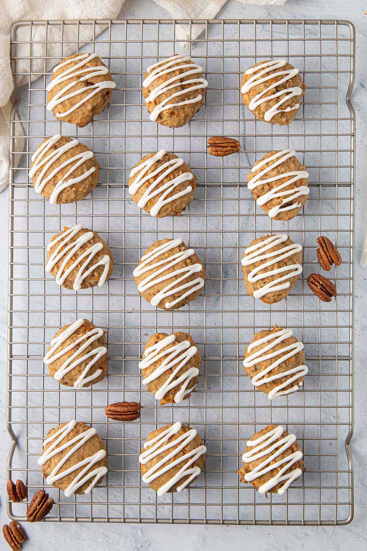 Carrot cake cookies on a wire rack with frosting drizzle and a few pecan halves around.