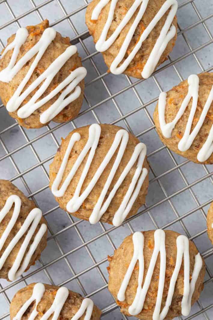 Close up of carrot cake cookies on a wire rack with a zig zag drizzle of icing on top of each cookie.