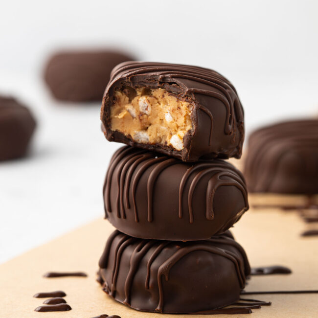 3 peanut butter eggs with chocolate coating stacked on top of each other with a bite taken out of the top egg.