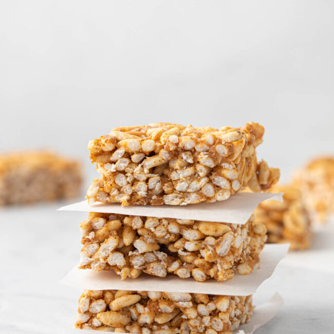 3 rice Krispie treats stacked on top of each other with a small square of parchment paper between each square.