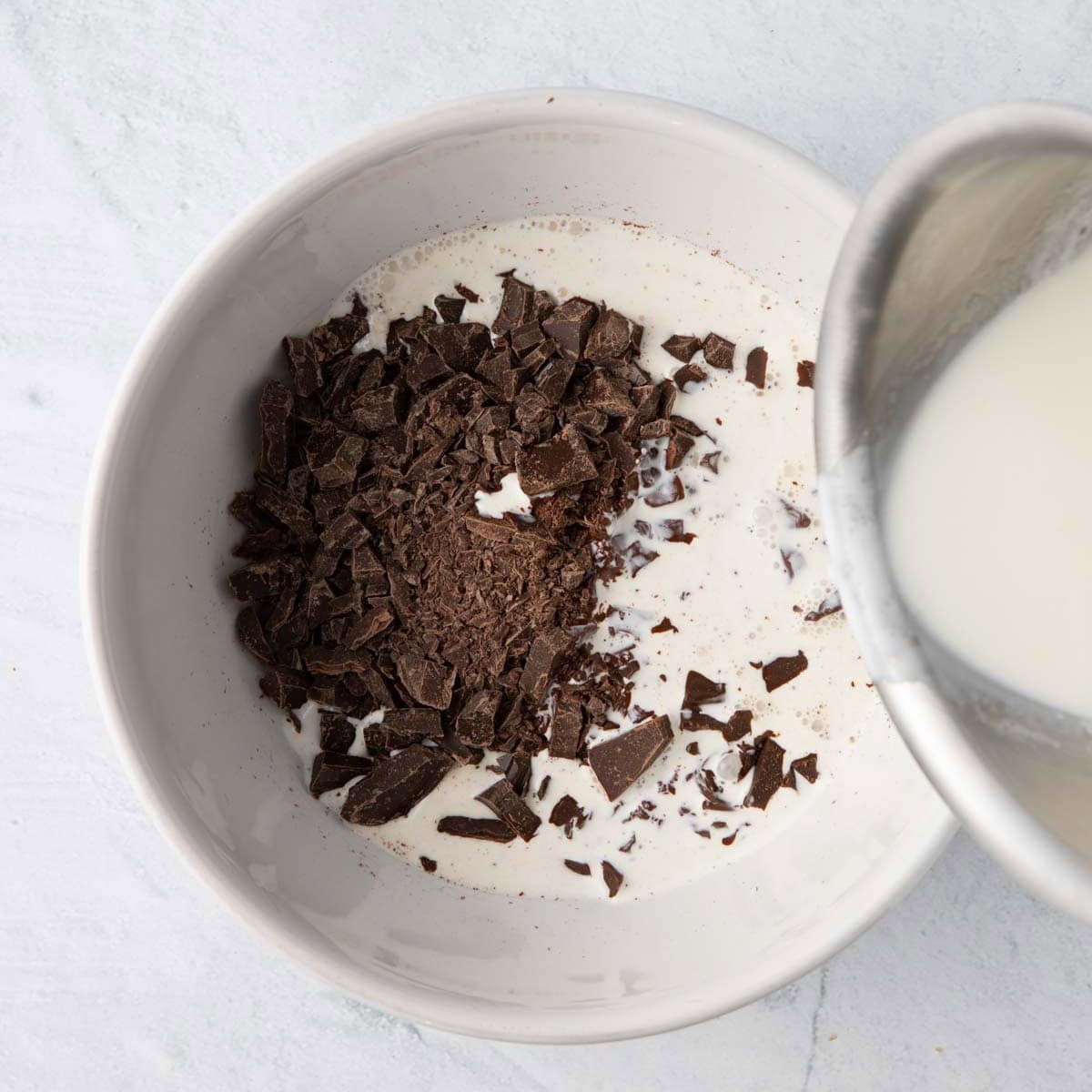 Finely chopped chocolate in a bowl with warm cream being poured over chocolate.