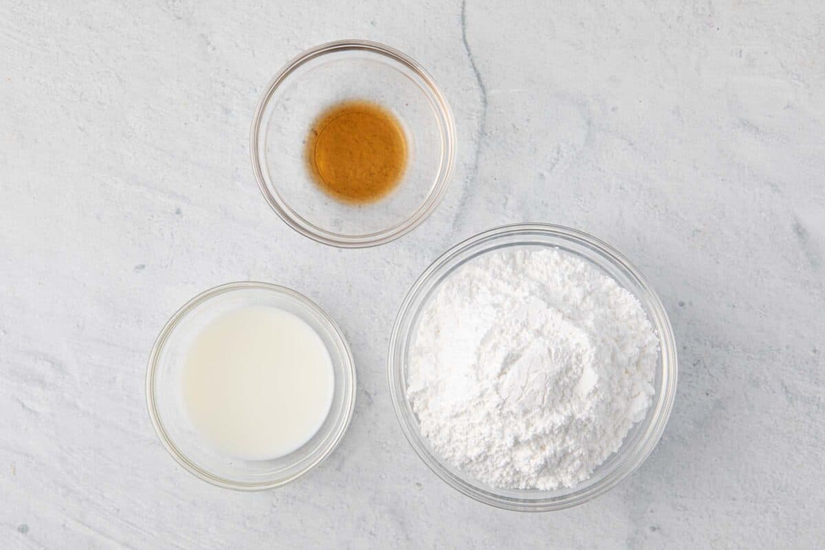 Ingredients for recipe in individual bowls: vanilla, milk, and powdered sugar.