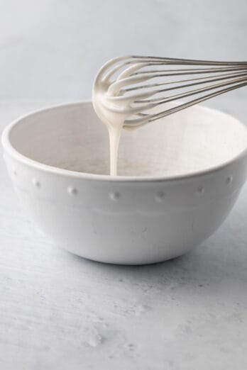 Whisk lifting up icing from a bowl with it falling back into it.