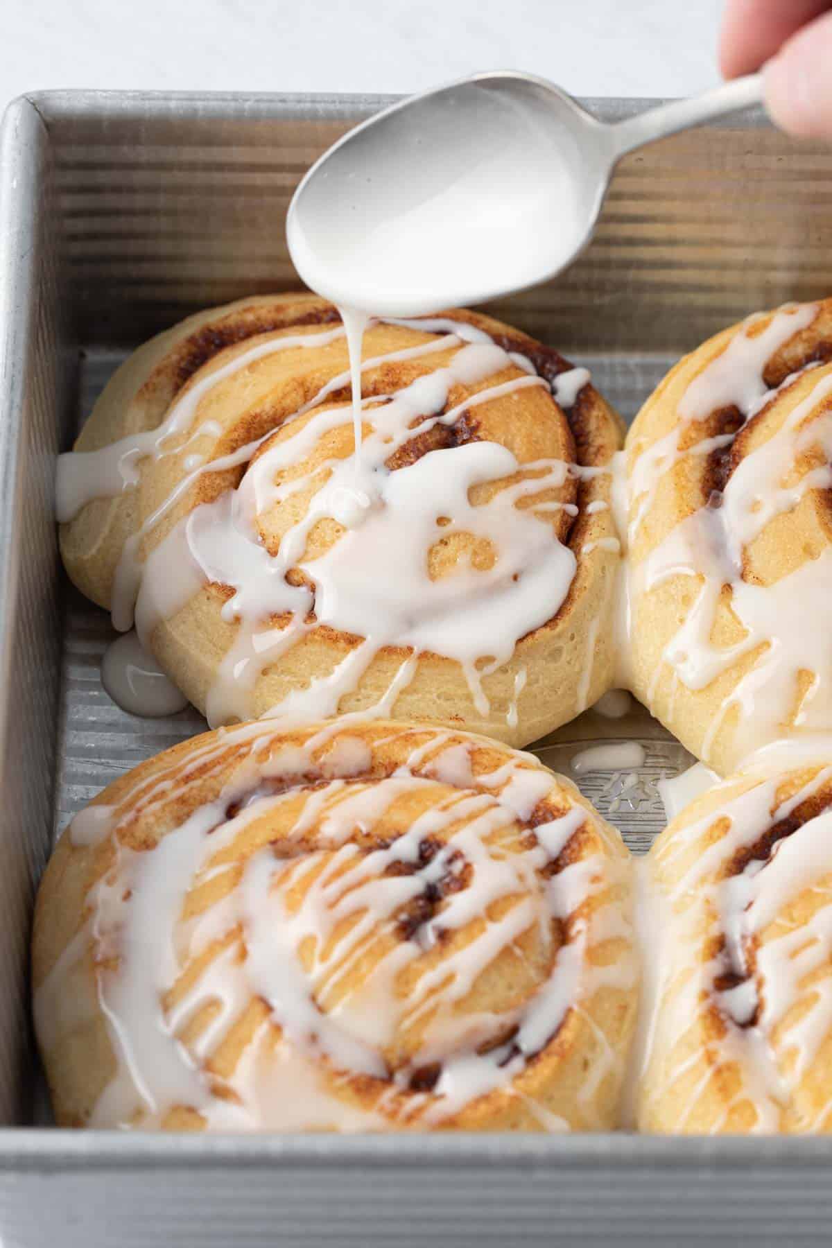 Icing being drizzled on top of cinnamon rolls in a baking dish.