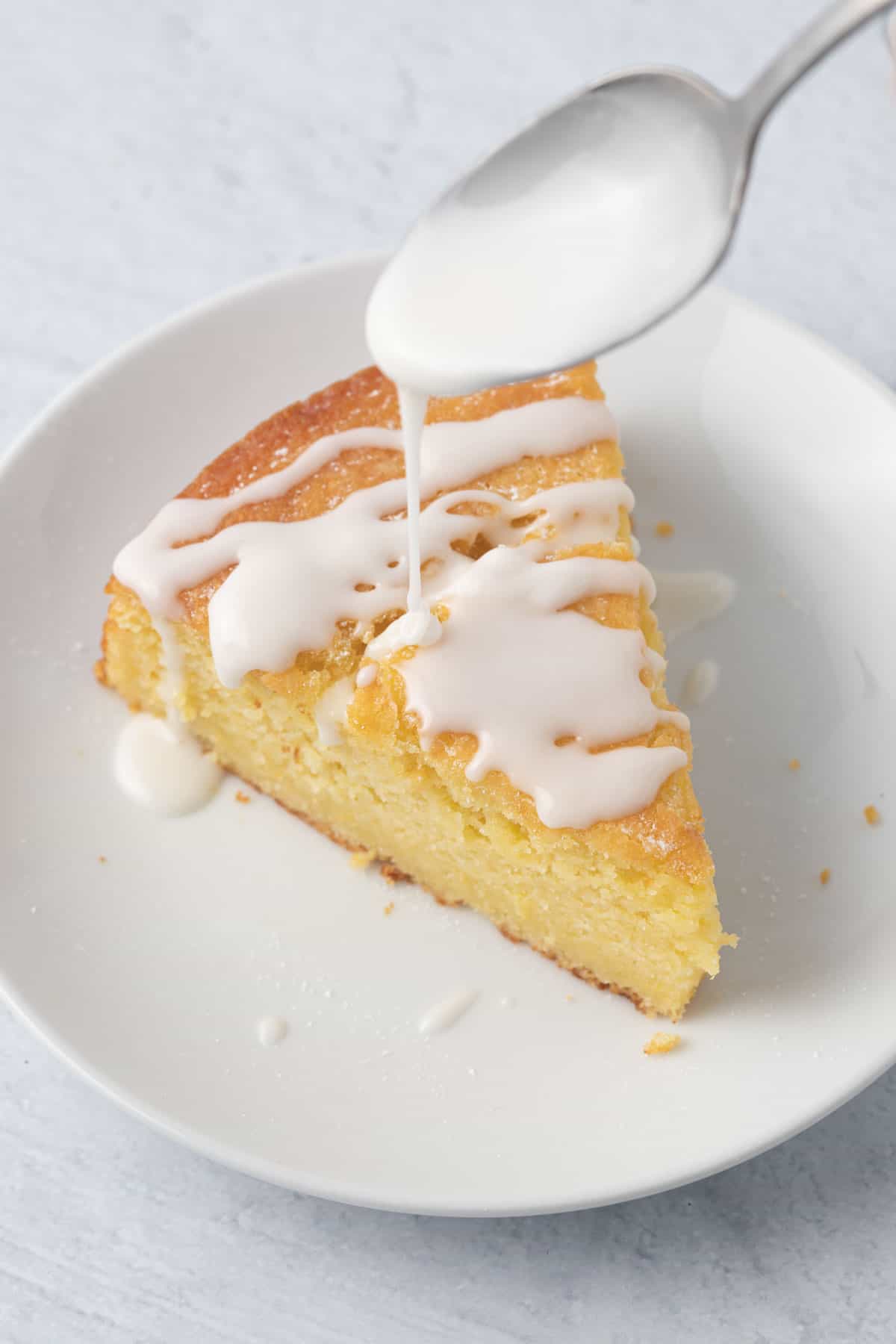 Icing being drizzled over a slice of lemon cake.