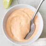 Spicy mayo in small bowl with spoon dipped and lime wedges off to the side.