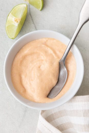 Spicy mayo in small bowl with spoon dipped and lime wedges off to the side.