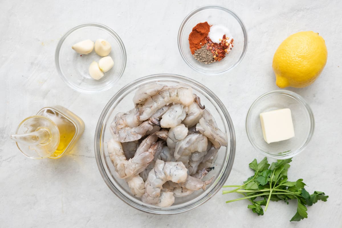 Ingredients for recipe before prepped: oil, garlic cloves, peeled and deveined shrimp, spices, whole lemon, butter, and parsley.
