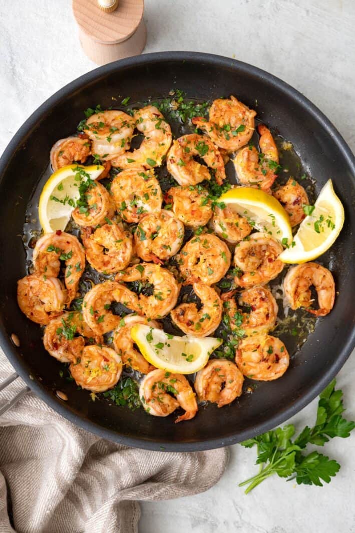 Shrimp in pan with lemon zest and squeezed lemon wedge, garnished with chopped fresh parsley.