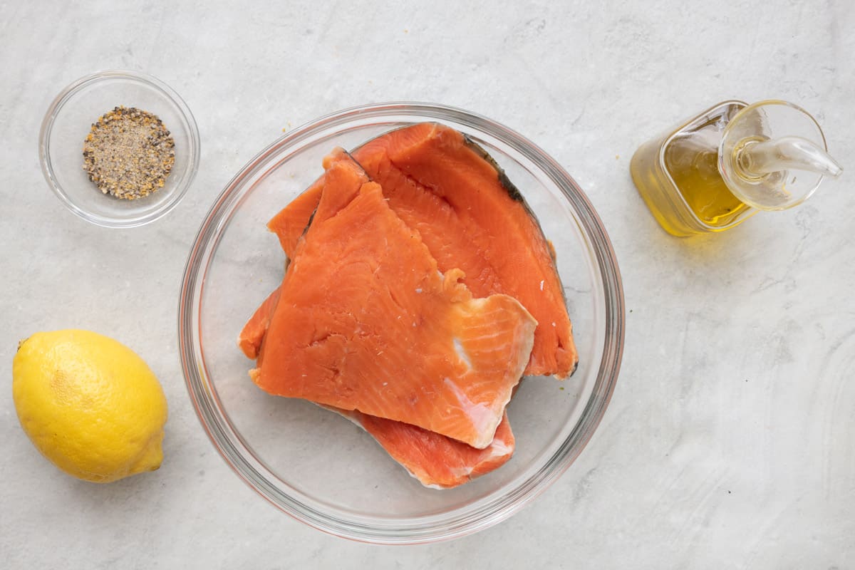 Ingredients for recipe: lemon pepper seasoning, lemon, salmon filets in bowl, and oil.