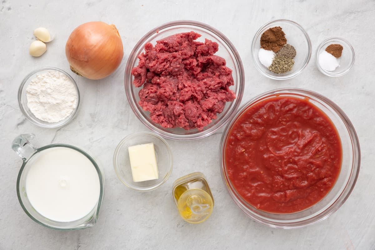 Ingredients for recipe: garlic cloves, flour, milk, onion, butter, ground beef, oil, spices, and crushed tomatoes.